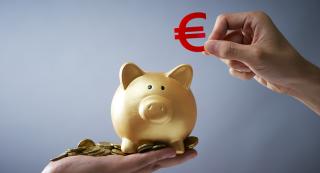Une main s'apprête à glisser un symbole euro dans une tirelire cochon posée sur une autre main pleine de pièces de monnaie
